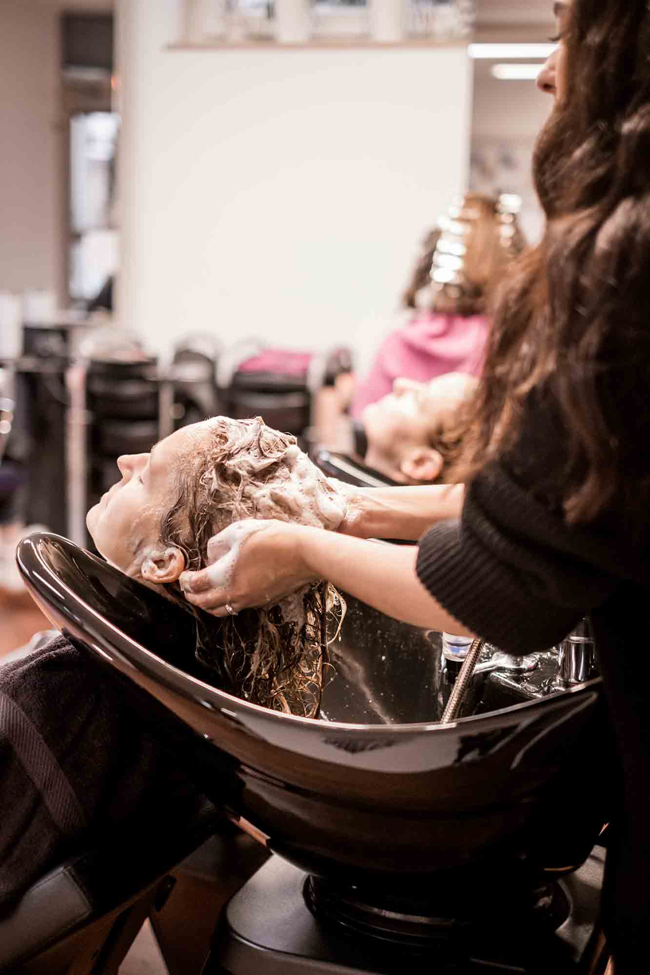 Friseurin wäscht das Haar einer Kundin am Waschbecken